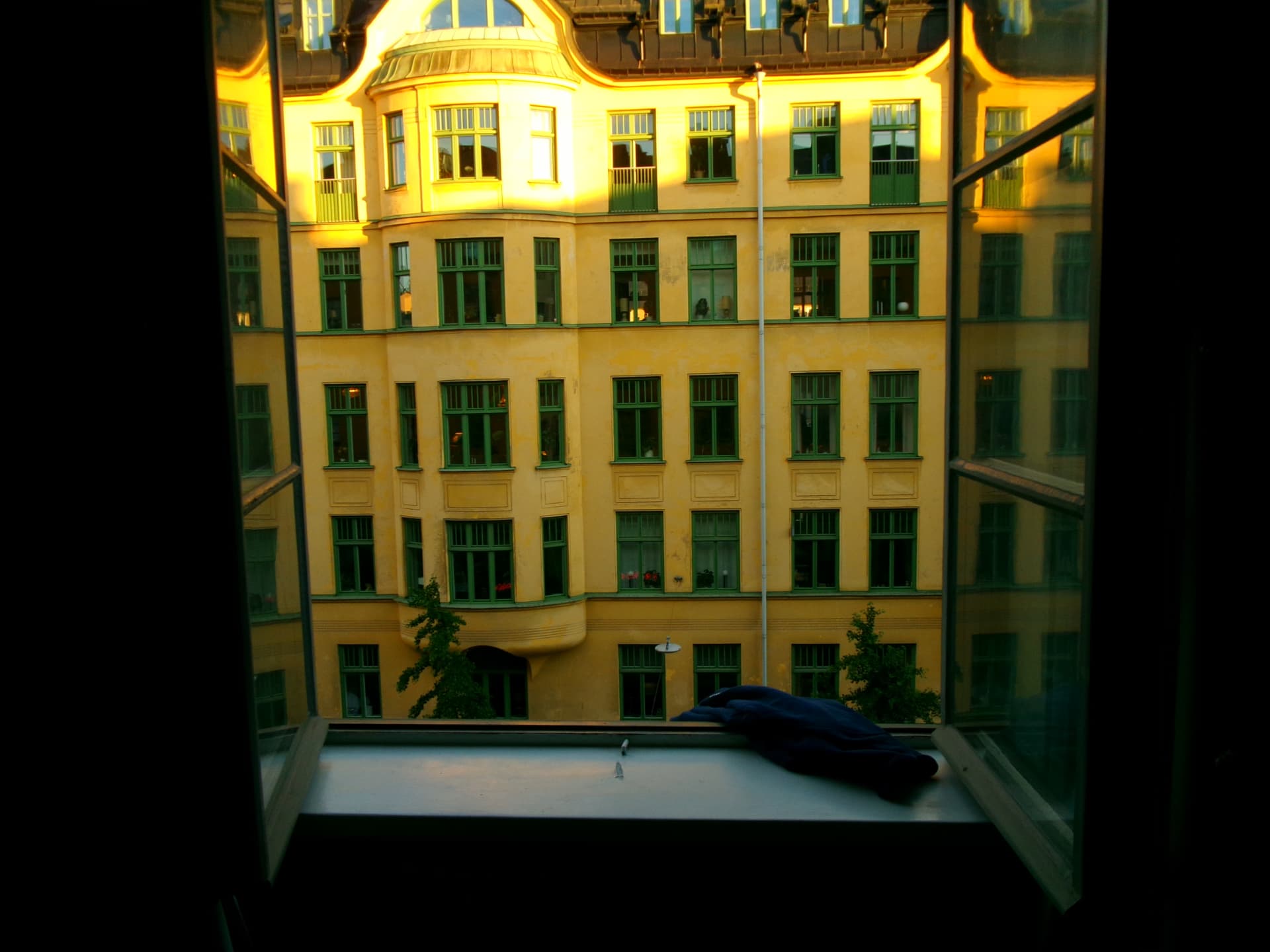 Evening light on a yellow courtyard facade seen through an open window